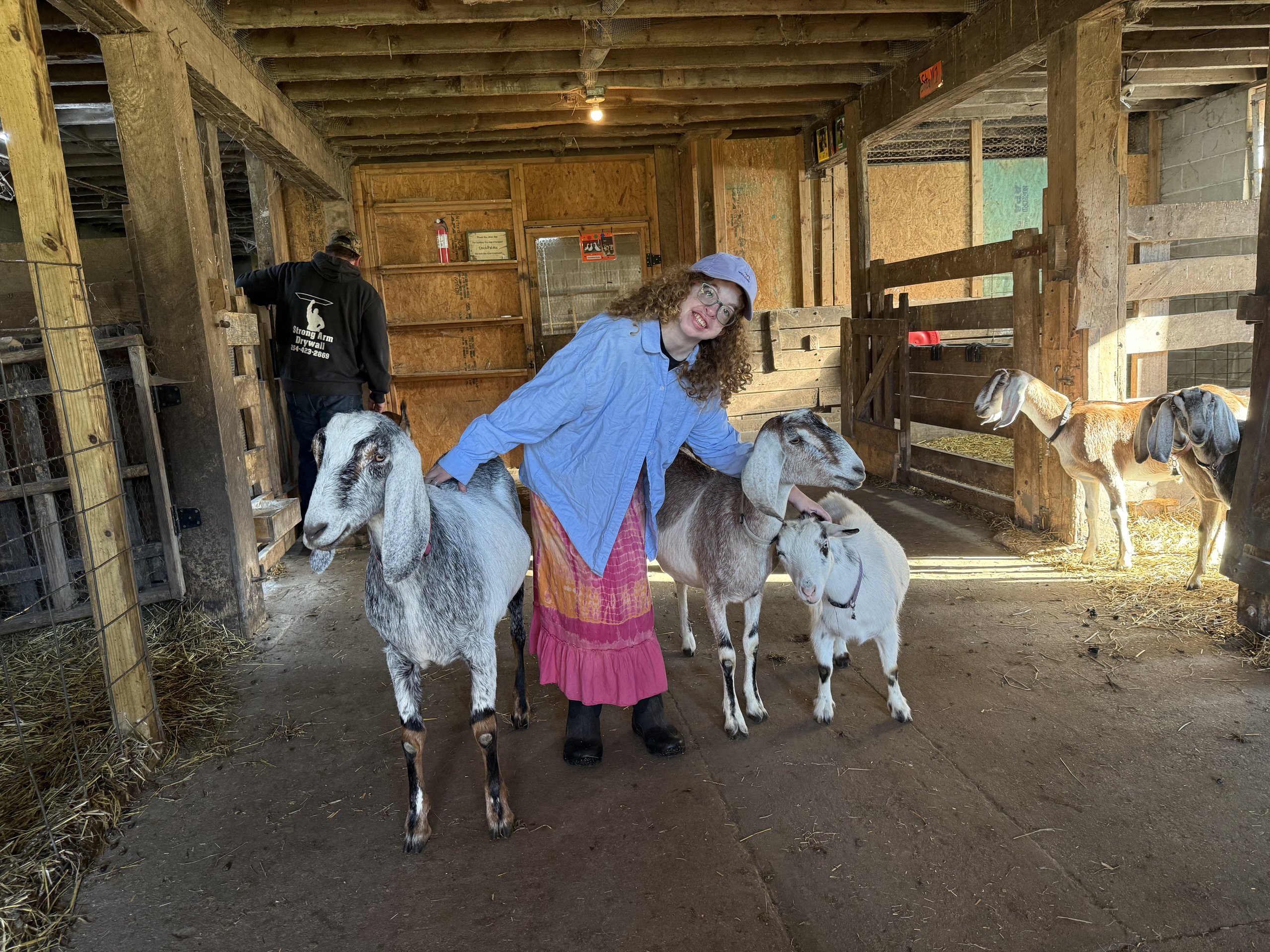 Participant smiling while standing with two goats at AACORN Farm.