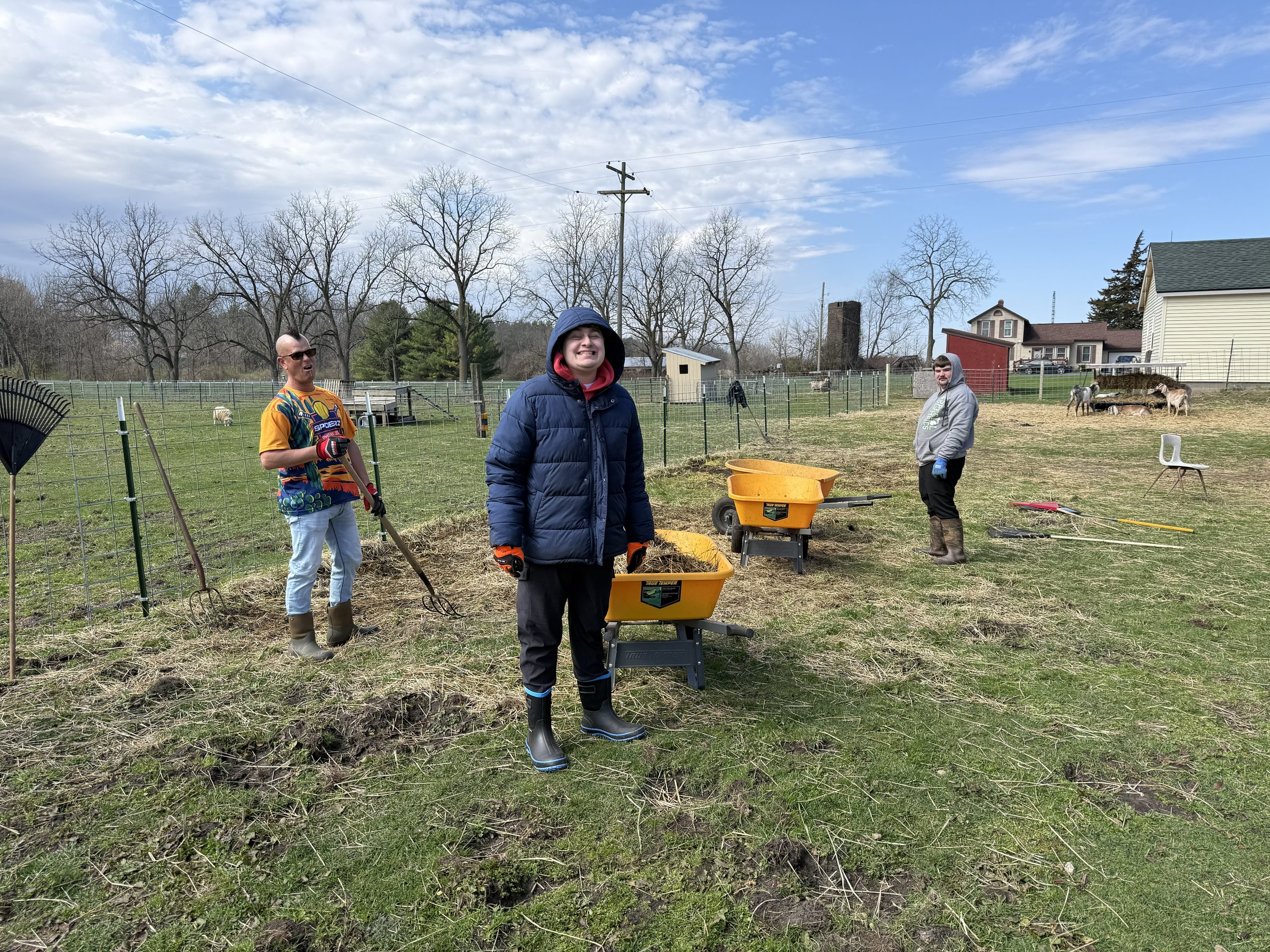 Participants and volunteers using rakes, pitchforks and wheelbarrows.