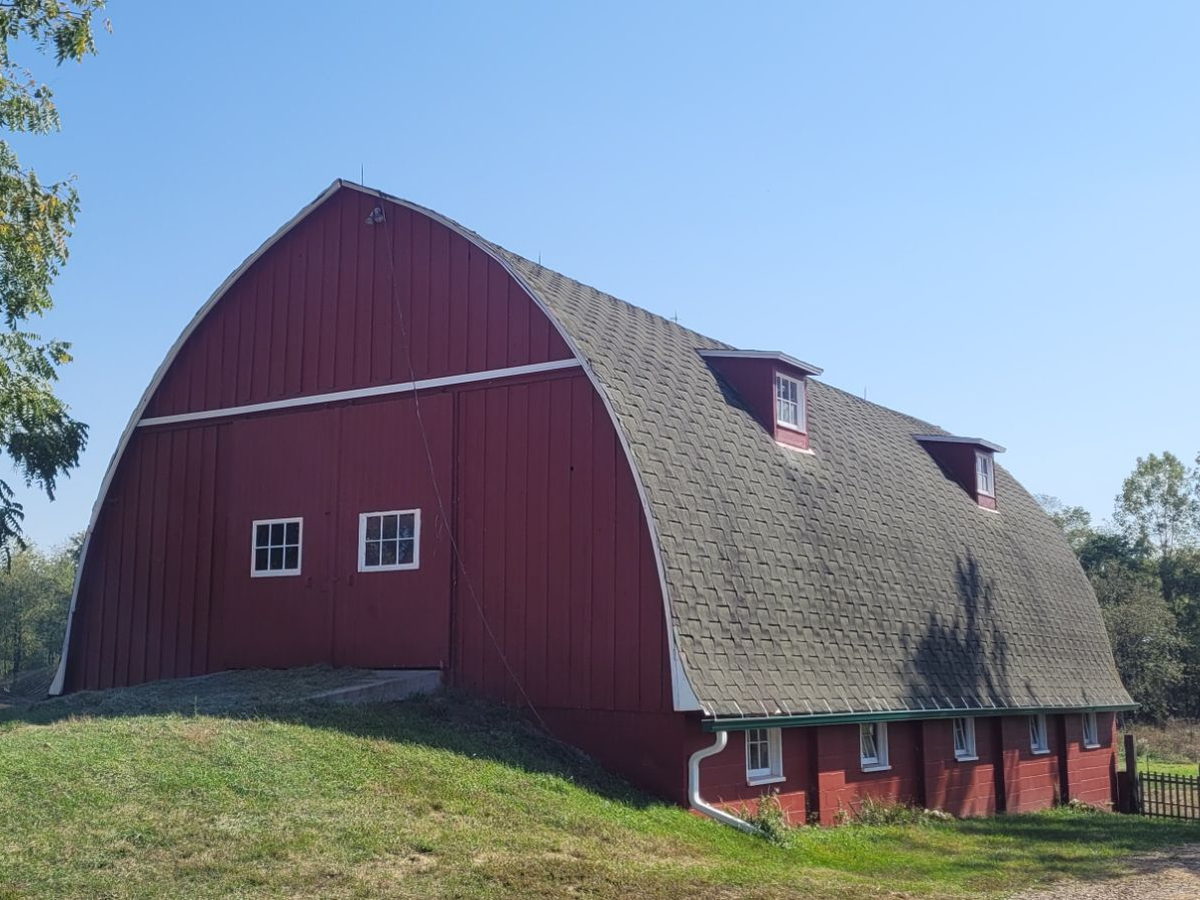 The restored red barn with its curved roof at AACORN’s 40-acre farm, under a clear blue sky.
