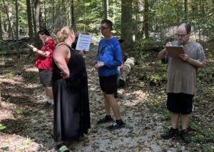 4 people in the woods looking at a scavenger hunt sheet